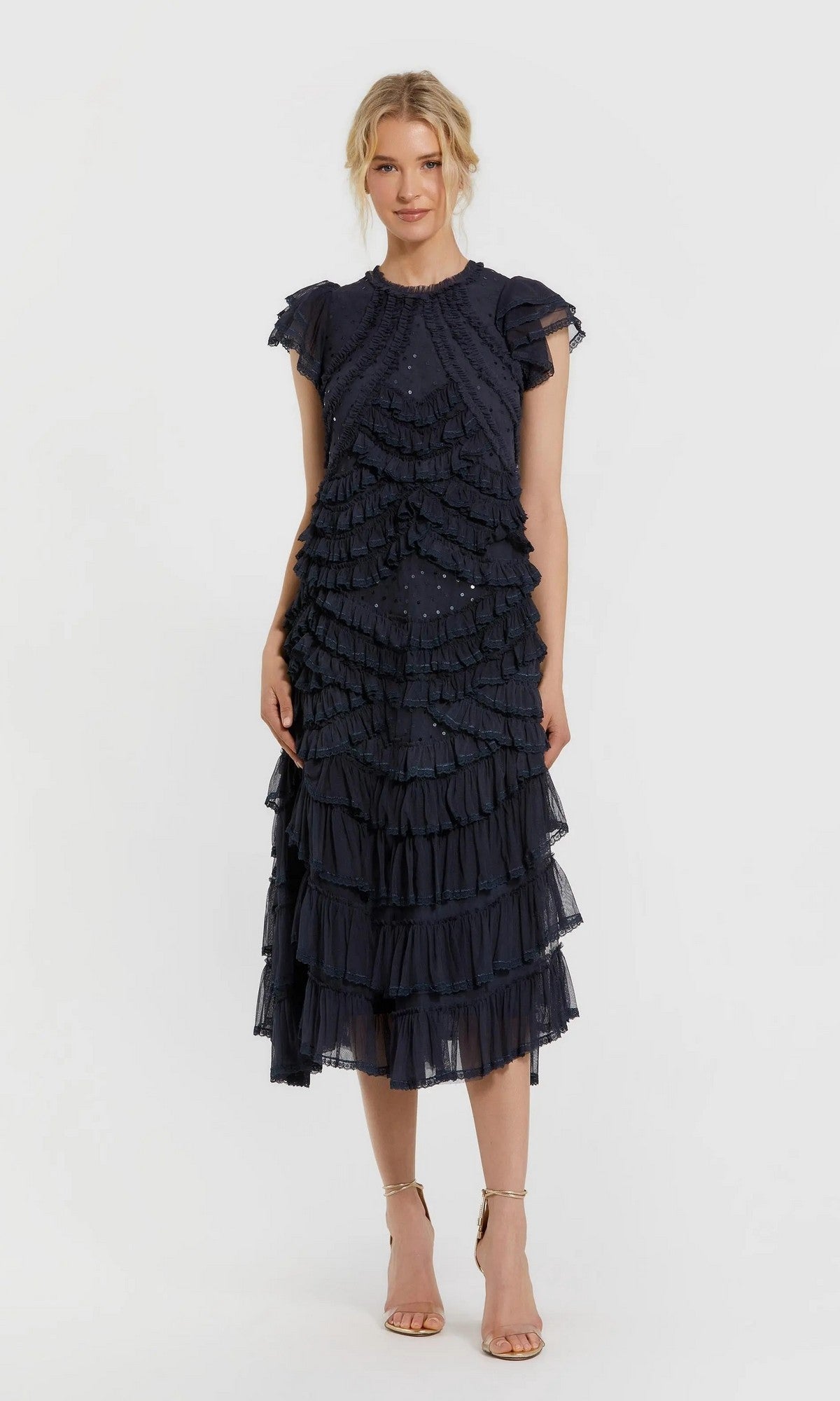 A woman wearing the Mac Duggal 8371 navy midi party dress, featuring a high neckline, micro-ruffle detailing, and flutter sleeves, paired with strappy nude heels and standing against a plain white background.